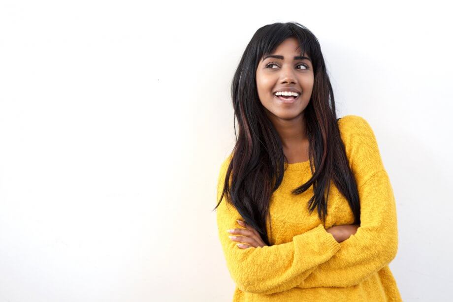 Woman with long dark hear wearing a yellow sweater smiling.