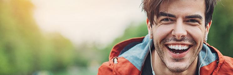 Man with orange and blue jacket wearing earbuds, smiling outside